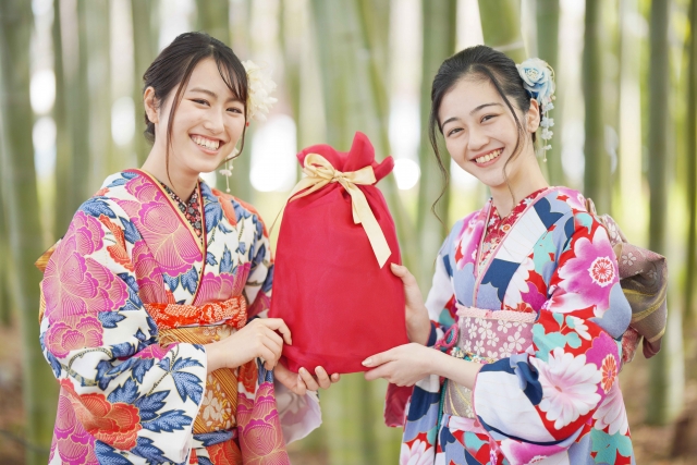 振袖姿の新成人ふたりが、赤い包みのお祝いの品を手渡しする様子